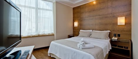 Habitación de hotel con cama, televisor, mesita de noche con control remoto y cabecero de madera.