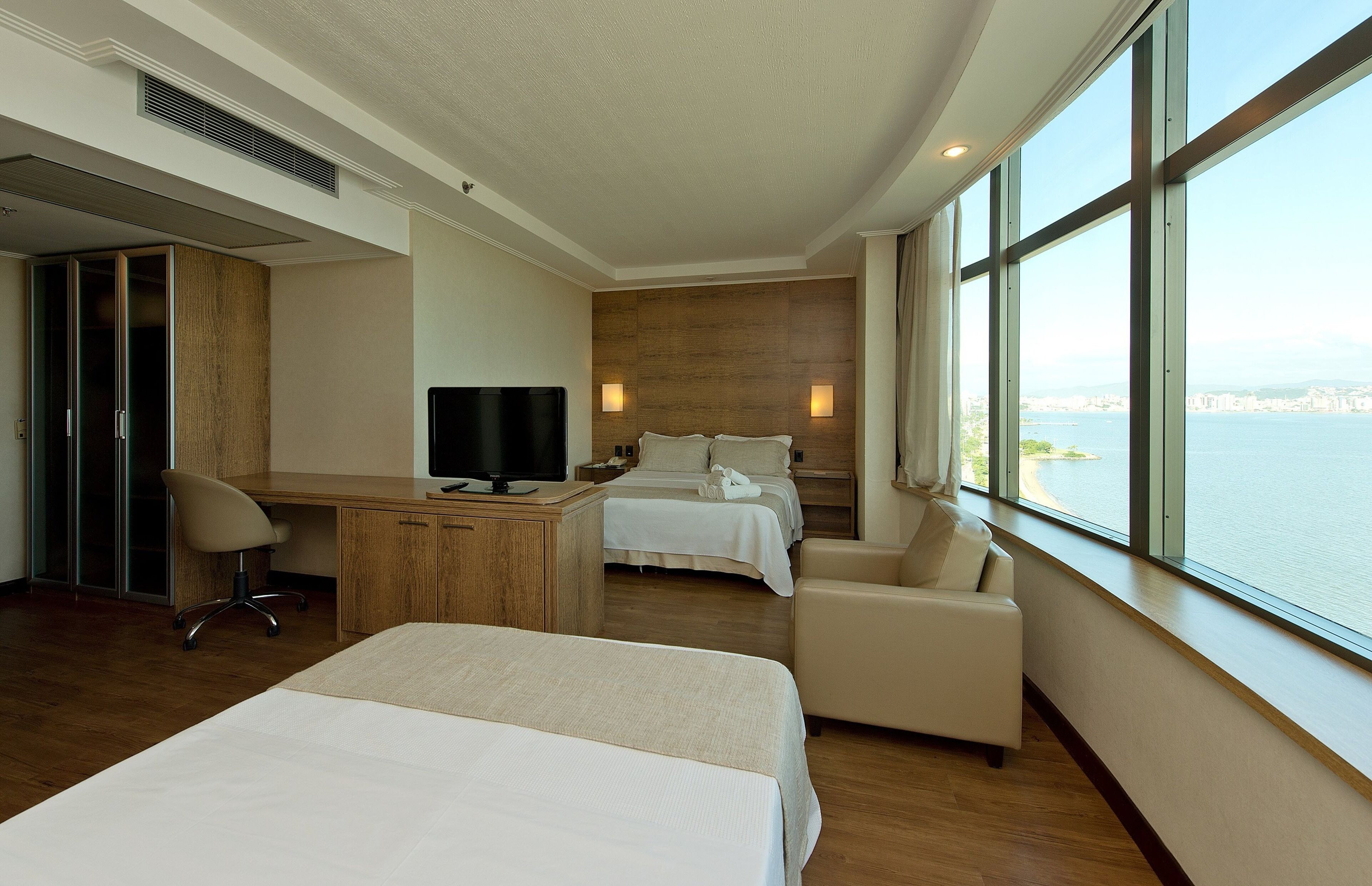 A hotel room with a large bed, a desk, a chair, and a view of the water.