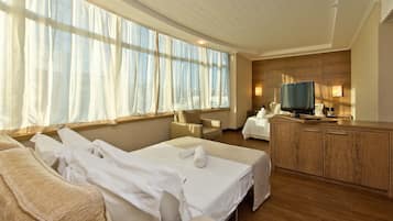 A hotel room with a large bed, a TV, a wooden cabinet, and a window with sheer curtains.