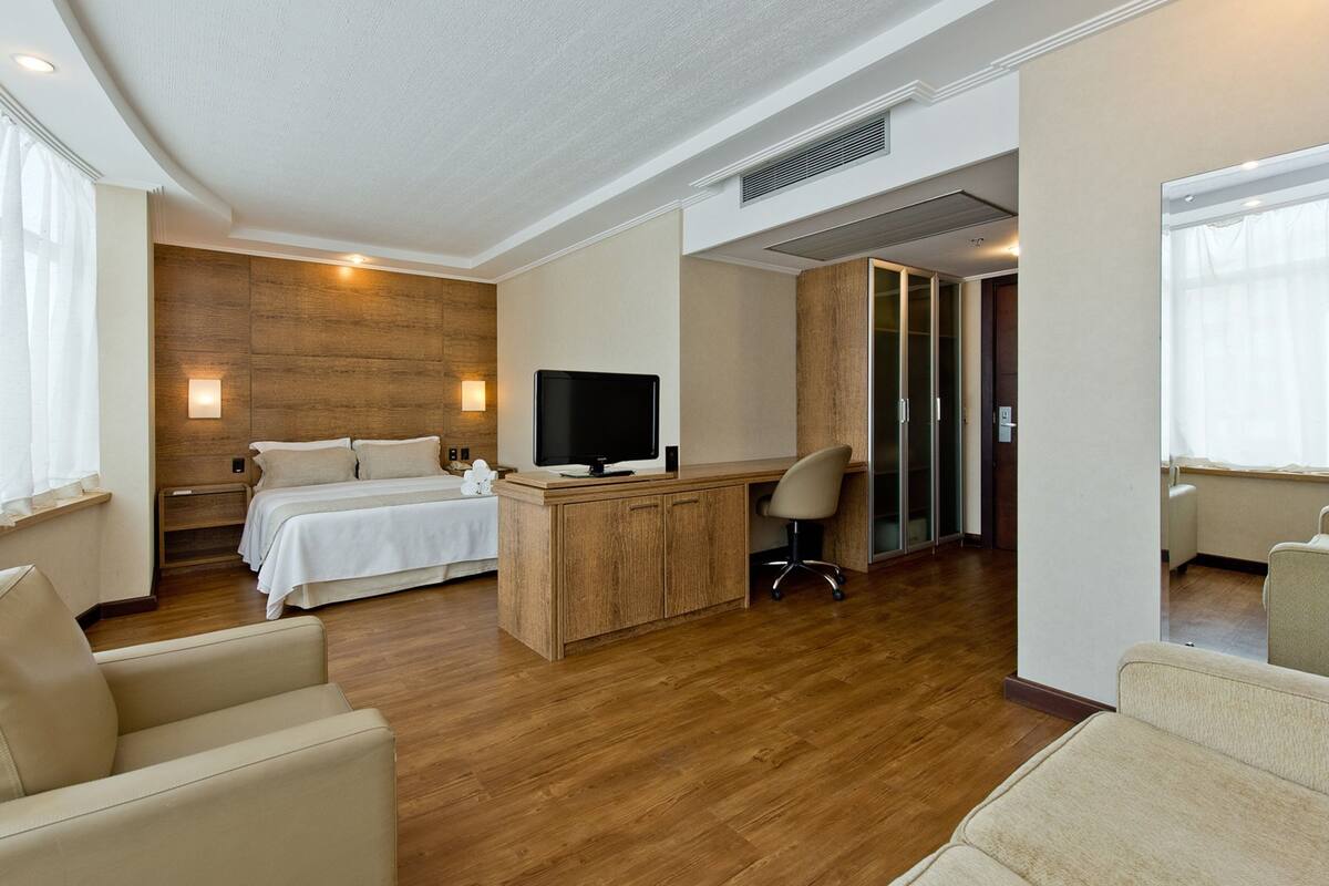 A hotel room with a bed, a desk with a computer, a TV, and a chair.