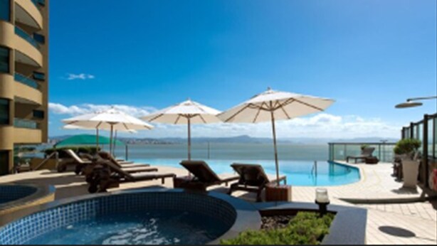 Un espace piscine avec des chaises longues et des parasols, un jacuzzi et une vue sur la mer.