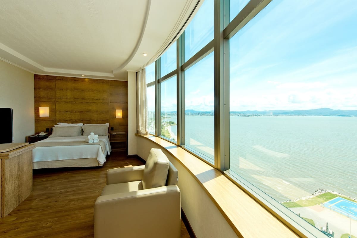 A hotel room with a large window, a bed, a desk, and a chair.