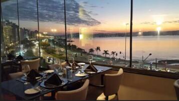 A dining area with a table set for two, overlooking a waterfront with a cityscape in the background.