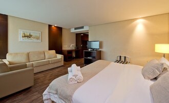 Una camera d'albergo con un letto, un divano, una TV e una scrivania.