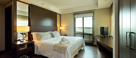 A hotel room with a large bed, a TV, a desk, and a window with a view.