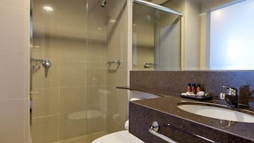 A modern bathroom with a glass-enclosed shower, a white toilet, and a granite countertop with a sink and mirror.