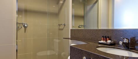 Ein modernes Badezimmer mit einer gläsernen Duschkabine, einer weißen Toilette und einer Waschtischplatte aus Granit mit Waschbecken und Spiegel.