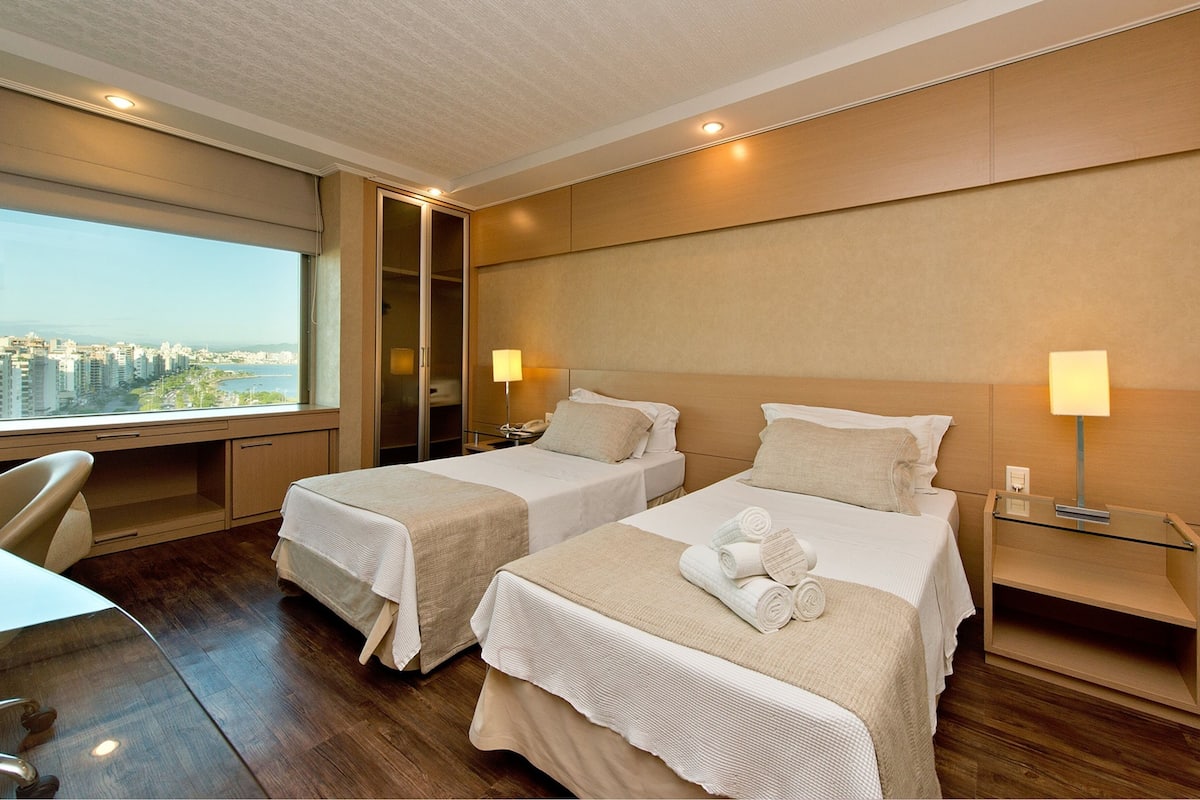 A hotel room with two beds, a desk, and a view of a cityscape.