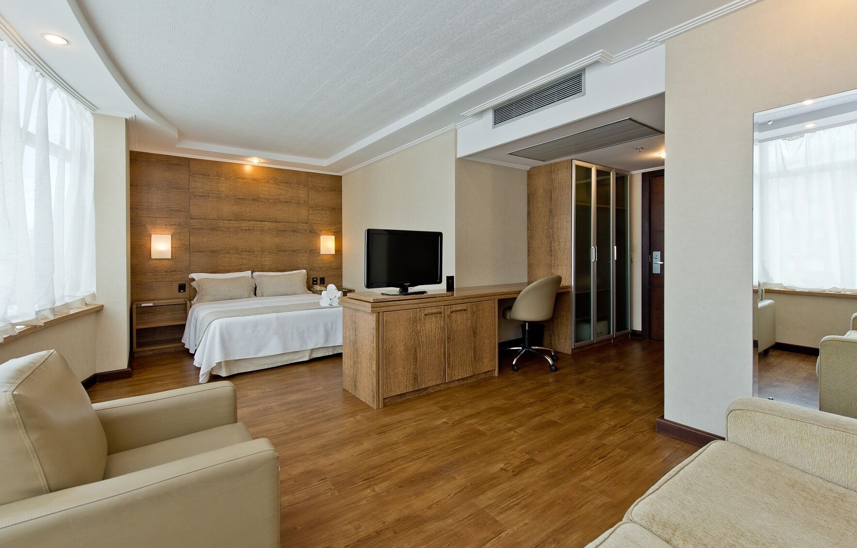 A hotel room with a wooden accent wall, a bed with white linens, a desk with a chair, and a television.