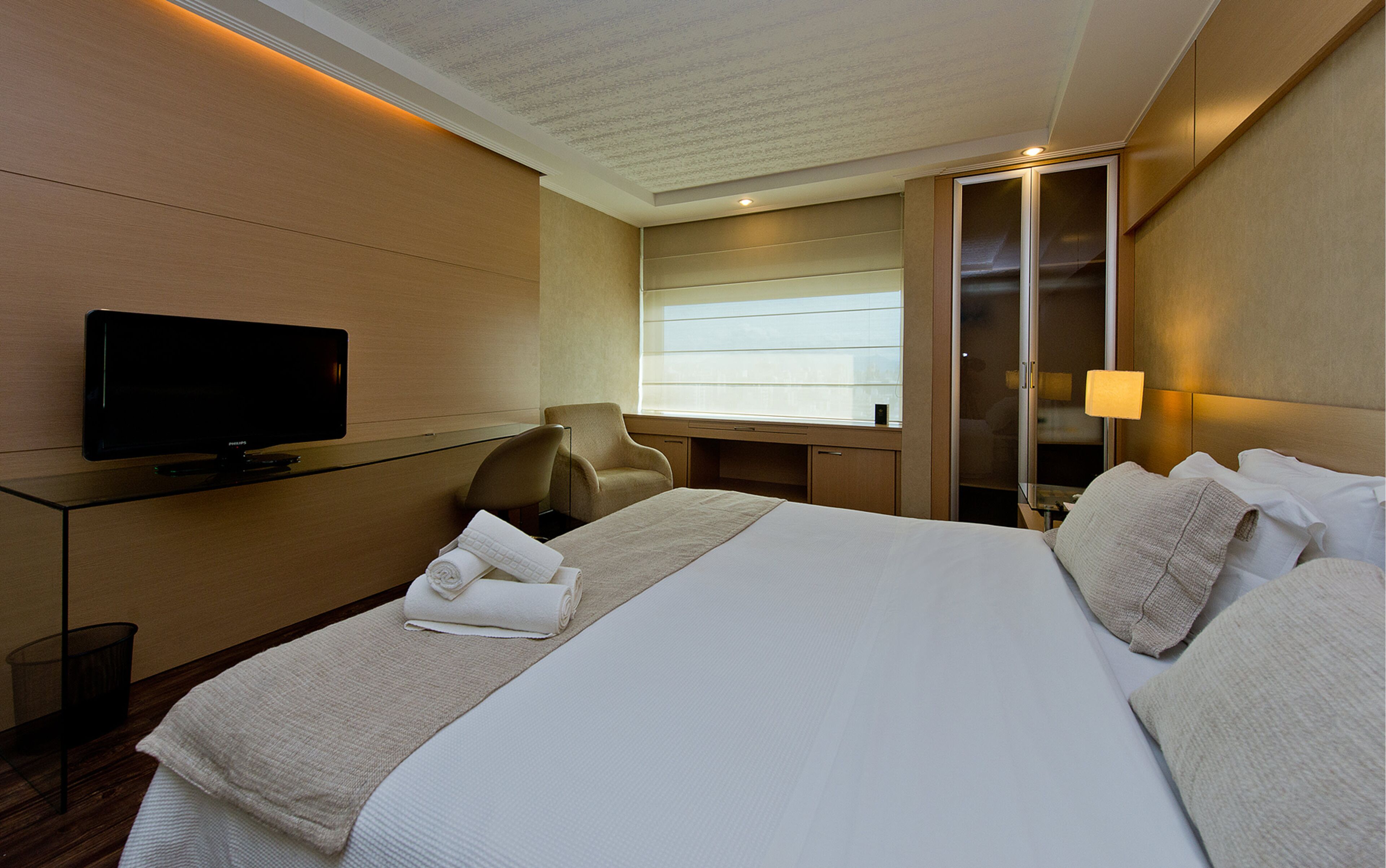 Quarto de hotel com cama, televisão, escrivaninha e cadeira.
