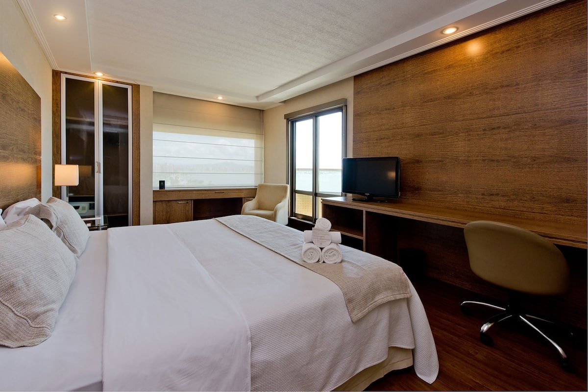 A hotel room with a large bed, a desk with a computer, a TV, and a chair.
