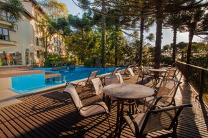 Area piscina con lettini e un tavolo, circondata da alberi e un edificio.