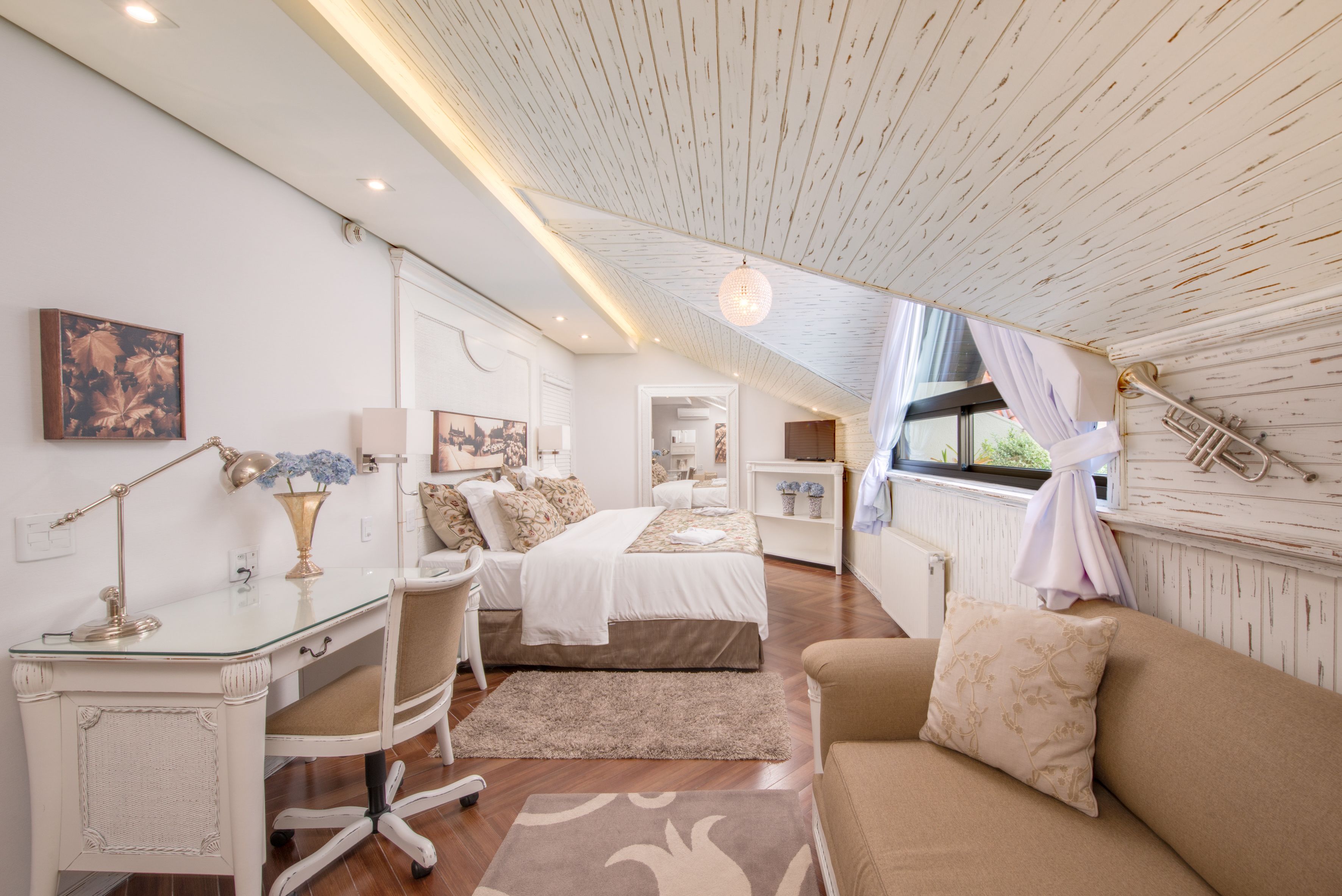 A bedroom with a bed, a desk, a chair, a couch, and a window with curtains.