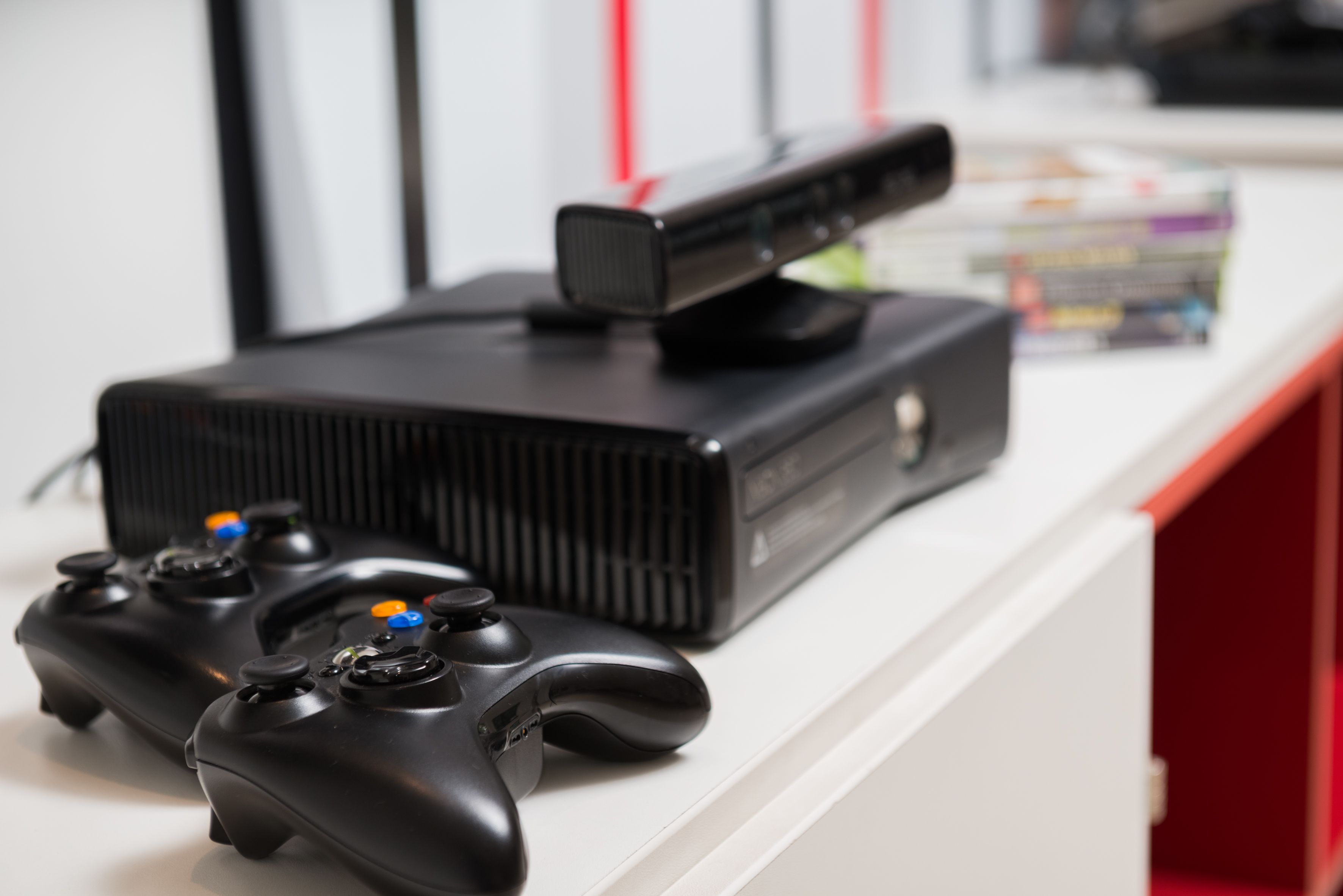 A gaming console and controller on a white surface with a red drawer in the background.