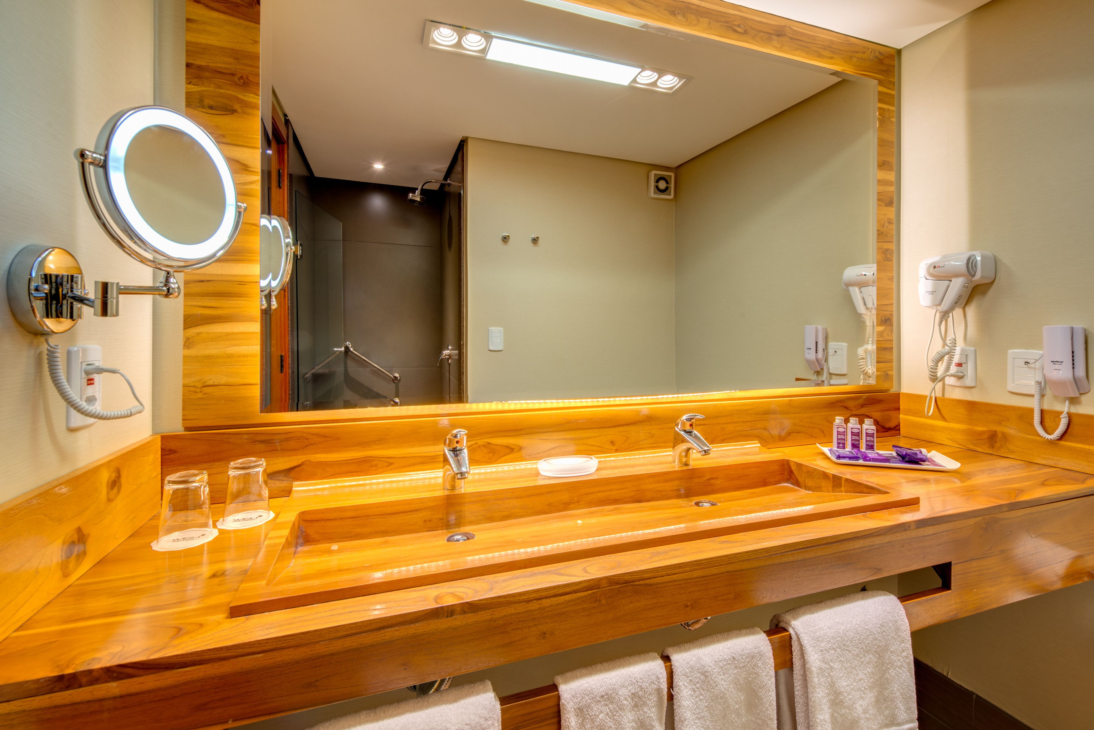 A wooden vanity with two sinks, a large mirror, and a hairdryer mounted on the wall.