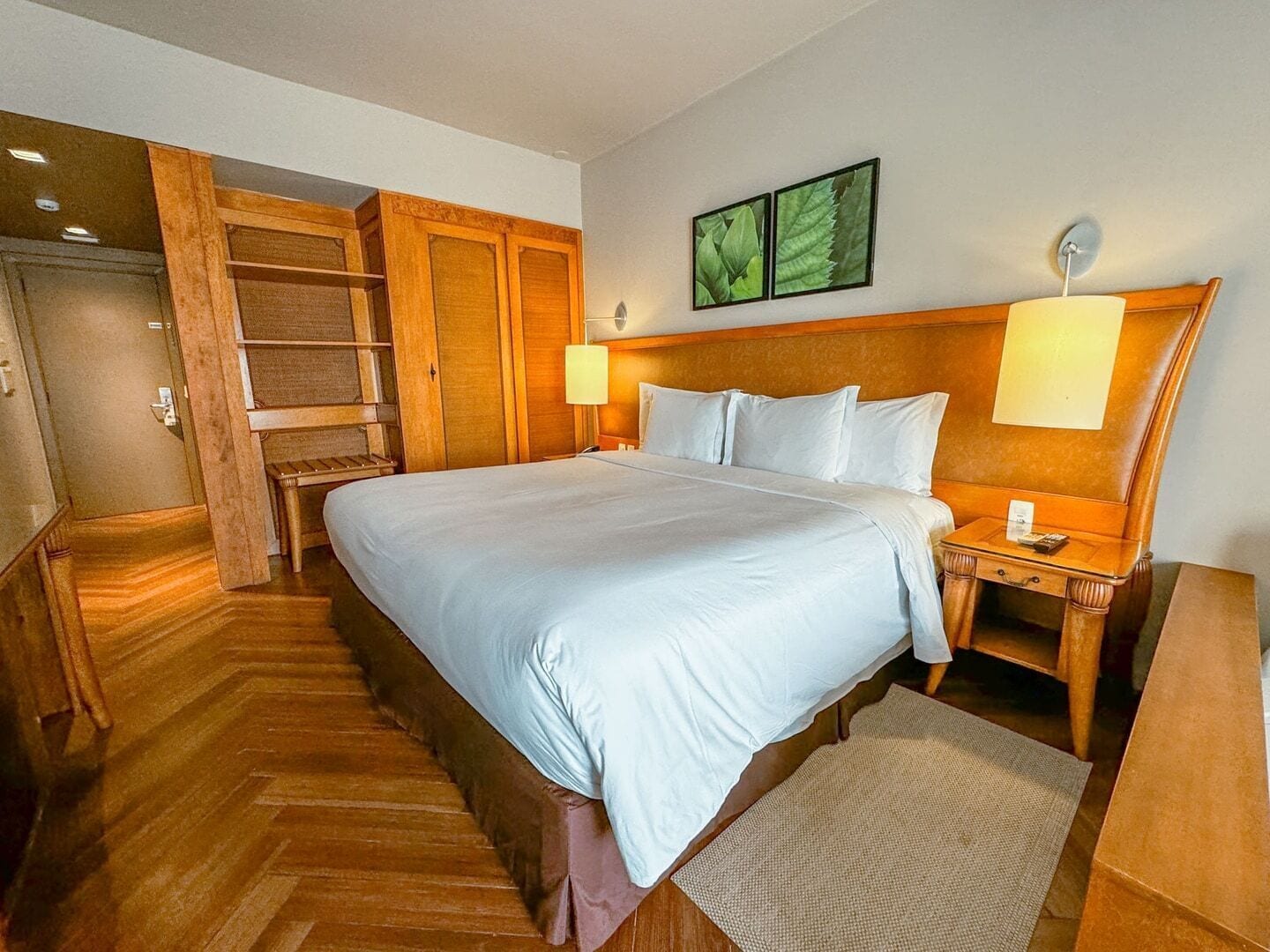 Une chambre d’hôtel avec un grand lit, une armoire en bois et une petite table de chevet avec une lampe.