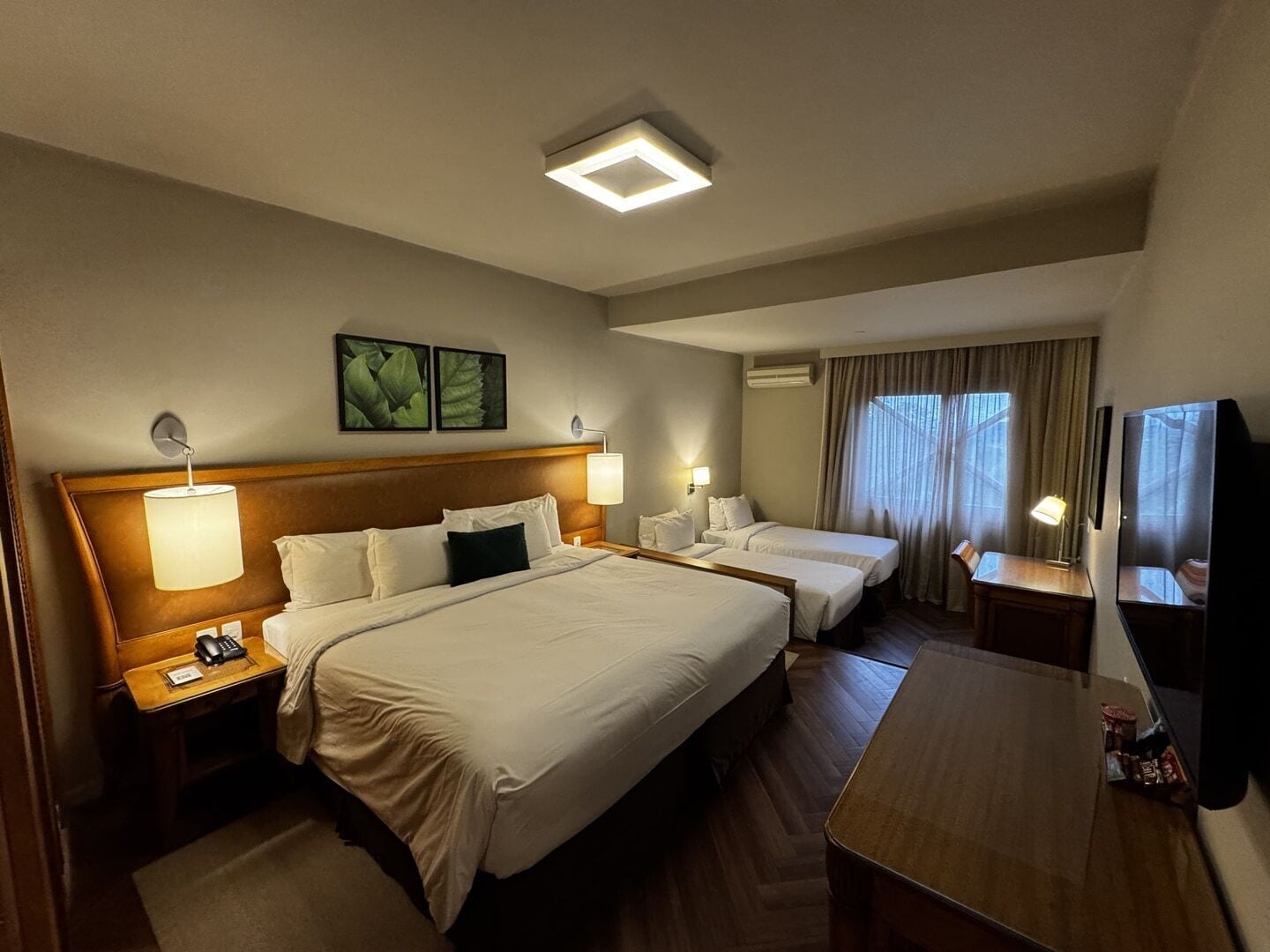 A hotel room with two beds, a desk, a TV, and a window with curtains.