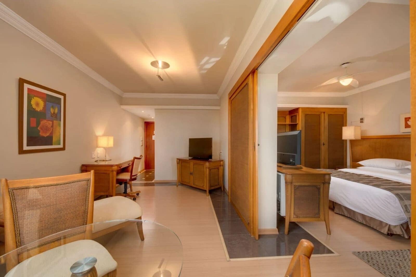 Habitación de hotel con cama, escritorio con computadora, televisión, silla y mesita.