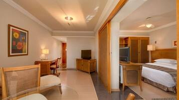 Habitación de hotel con cama, escritorio con computadora, televisión, silla y mesita.