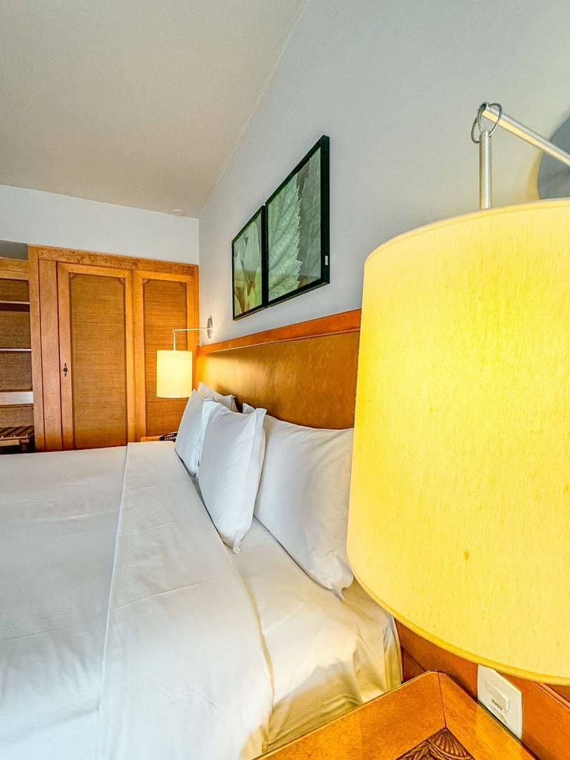 A hotel room with a large bed, wooden headboard, a nightstand with a lamp, and a framed picture on the wall.