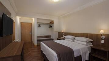 Quarto de hotel com cama, mesas de cabeceira, televisão e piso de madeira.