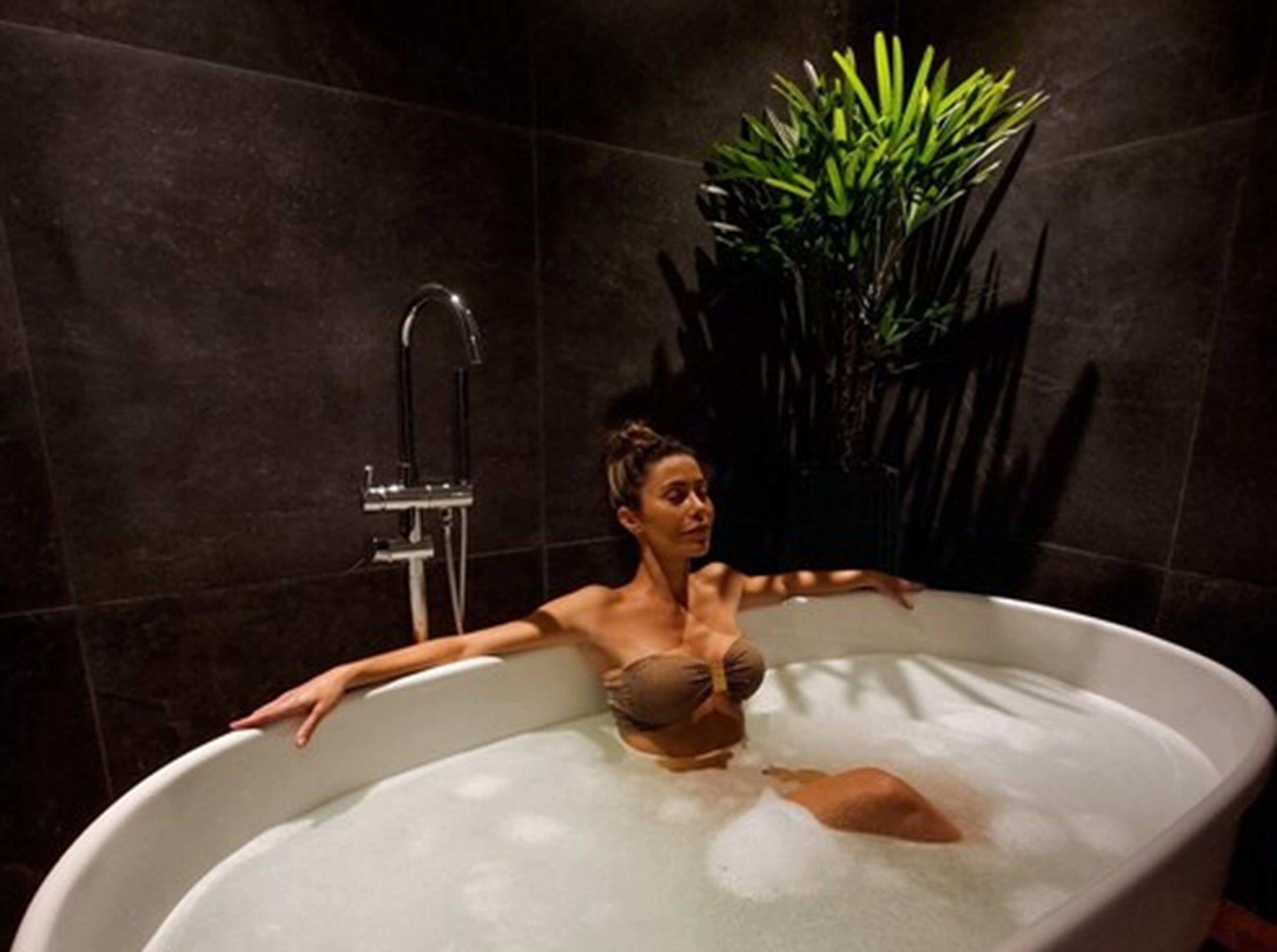 Una mujer se relaja en una bañera con una planta de fondo.