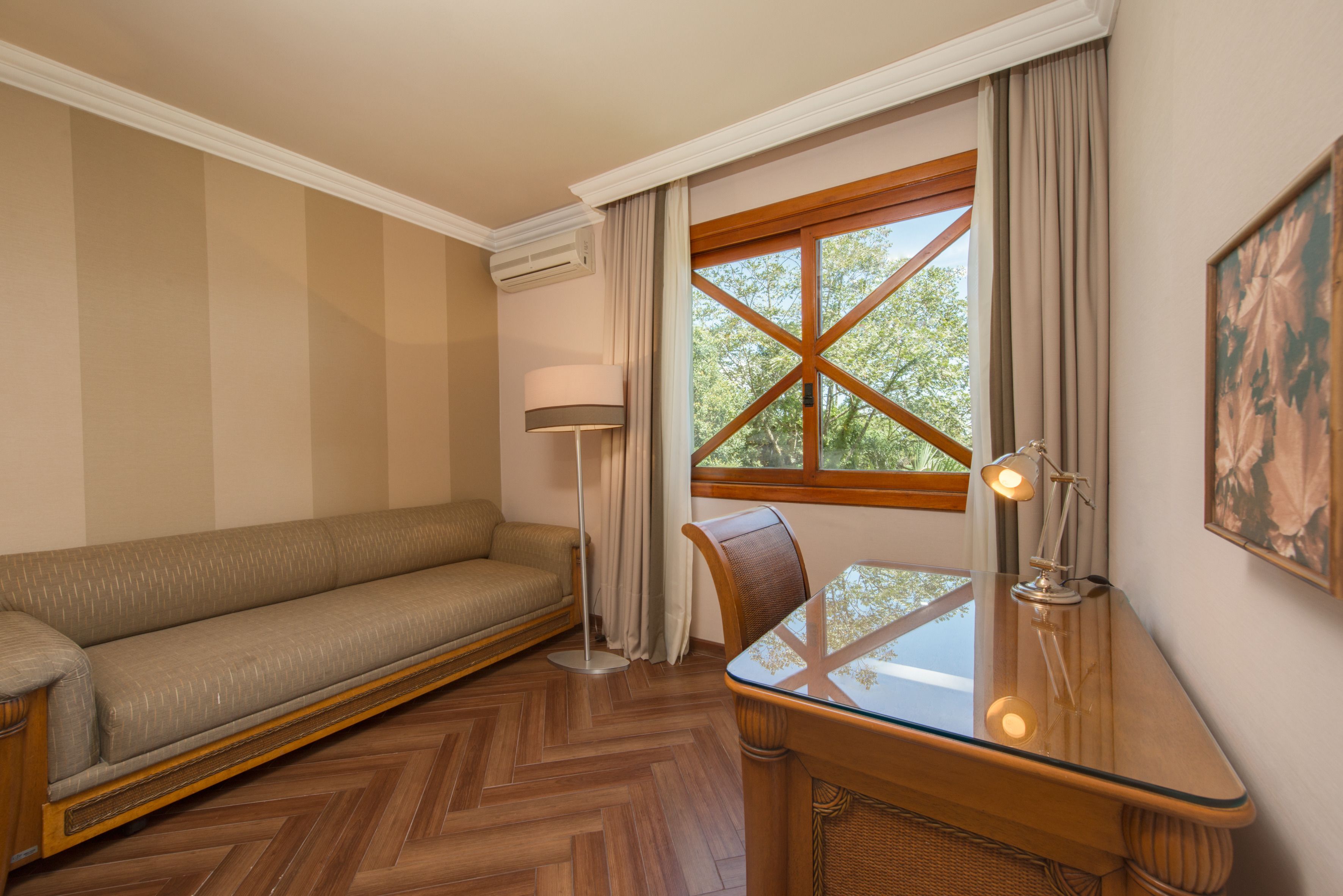 A room with a sofa, a glass-top table, a lamp, and a window with curtains.