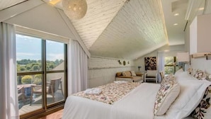 Une chambre dotée d’un grand lit, offrant une vue sur l’extérieur et dont le plafond présente un design original.