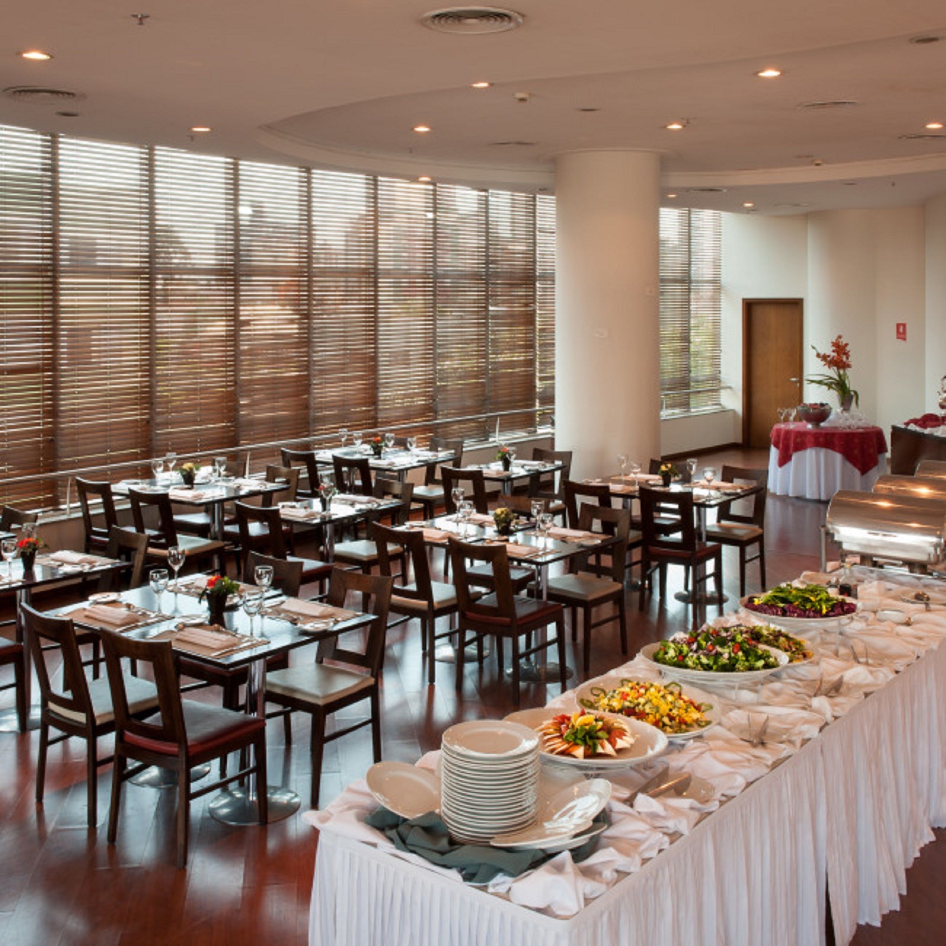 Un comedor amplio con varias mesas dispuestas para comidas, ventanas grandes y una barra de buffet con distintos platos.