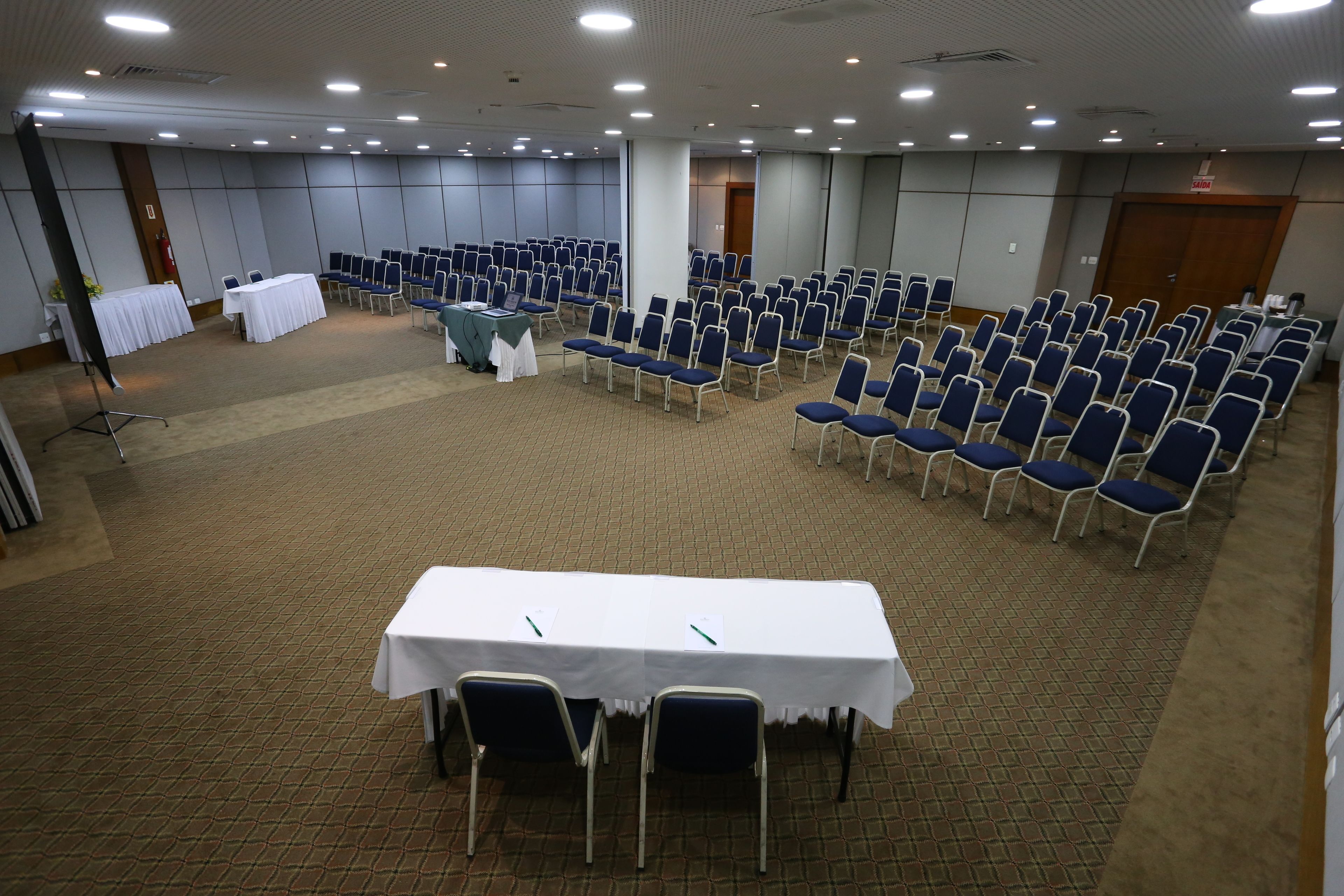 A conference room with rows of blue chairs and a white table.