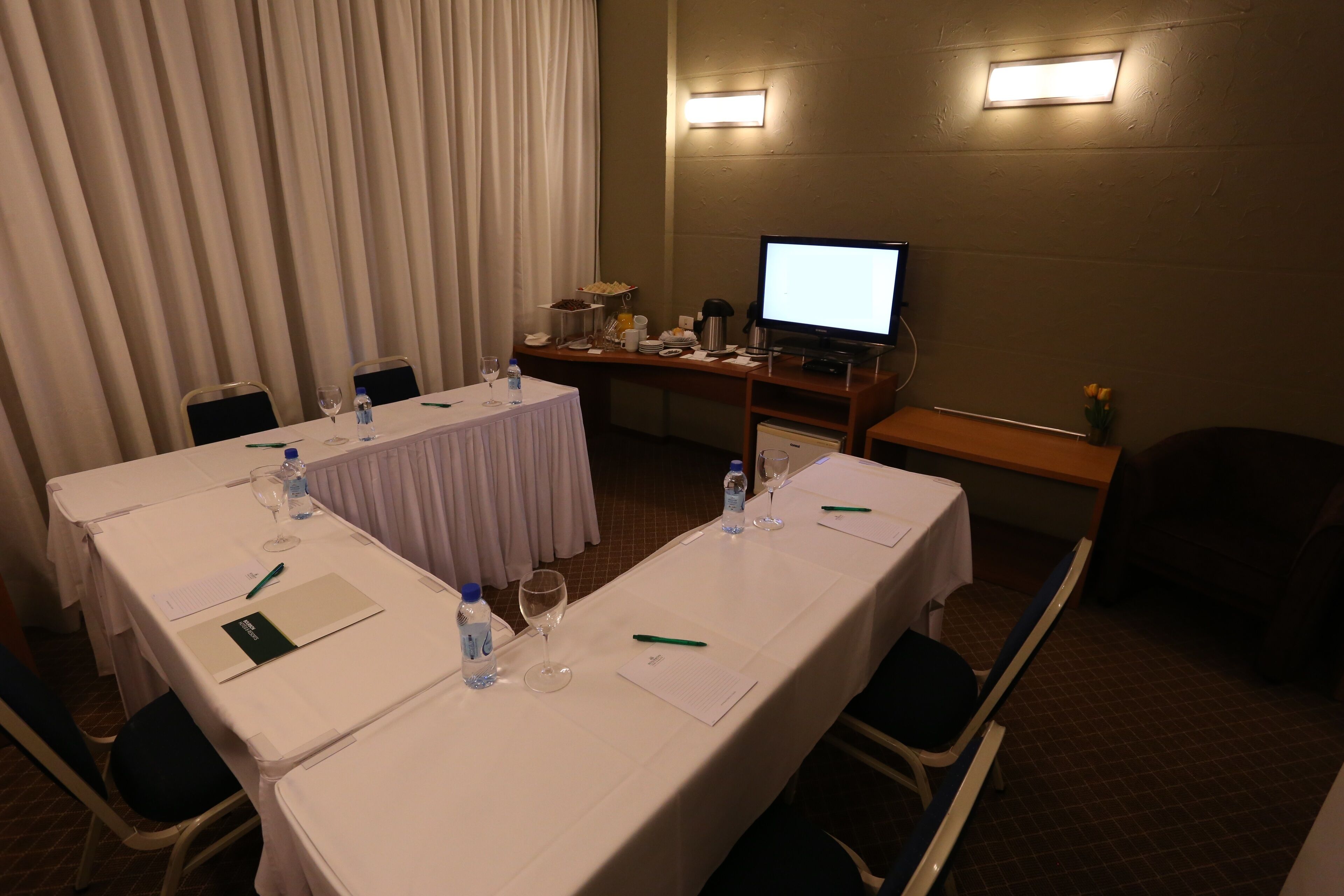 Una sala de conferencias con una larga mesa, sillas, una televisión y un escritorio pequeño con un ordenador.