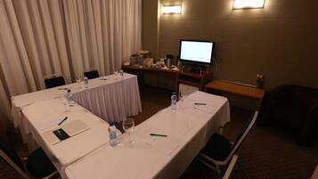 Una sala de conferencias con una larga mesa, sillas, una televisión y un escritorio pequeño con un ordenador.