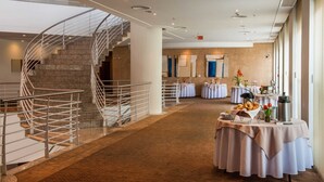 Un moderno vestíbulo de hotel con una escalera de caracol, varias mesas dispuestas para comer, y un gran ventanal que proporciona luz natural.