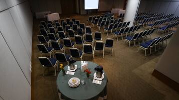 A conference room with rows of chairs, a projector screen, and a table with a floral arrangement and a coffee pot.