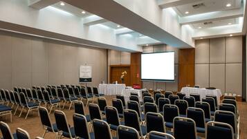 A conference room with rows of chairs, a projection screen, a whiteboard, and tables with nameplates.