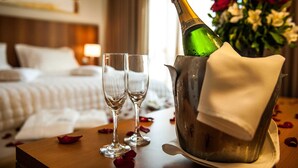 Habitación de hotel con cama, mesita de noche con una botella de champán, dos copas y un florero con flores.