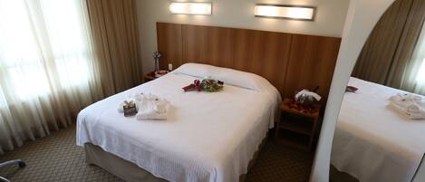 Una habitación de hotel con una cama grande, una mesita de noche, un espejo y una ventana con cortinas.