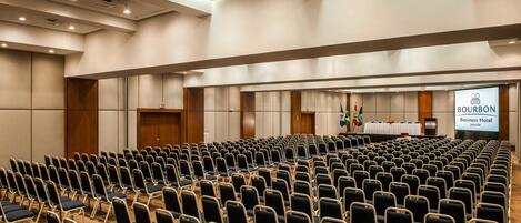 A conference room with rows of chairs, a podium, and a projection screen displaying "BOURBON Business Hotel".