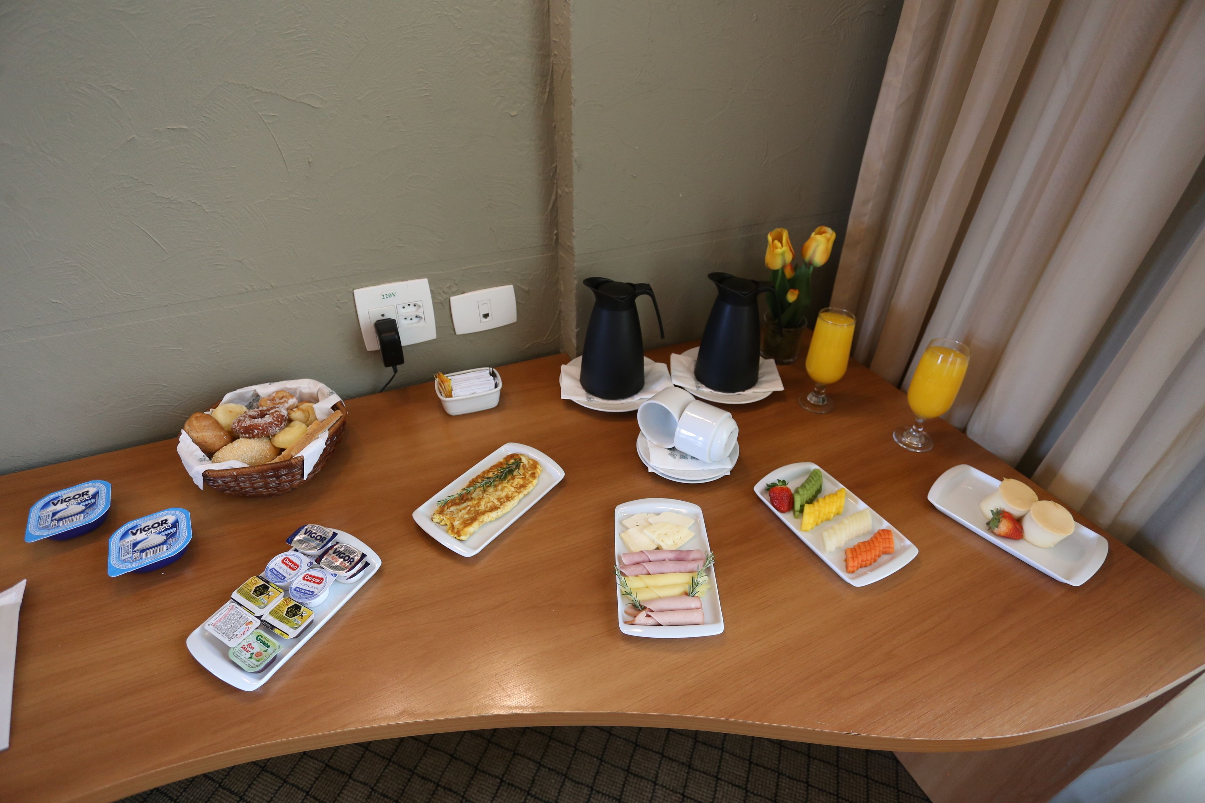 Um buffet de café da manhã com diversos alimentos, acompanhamentos e bebidas sobre uma mesa de madeira.