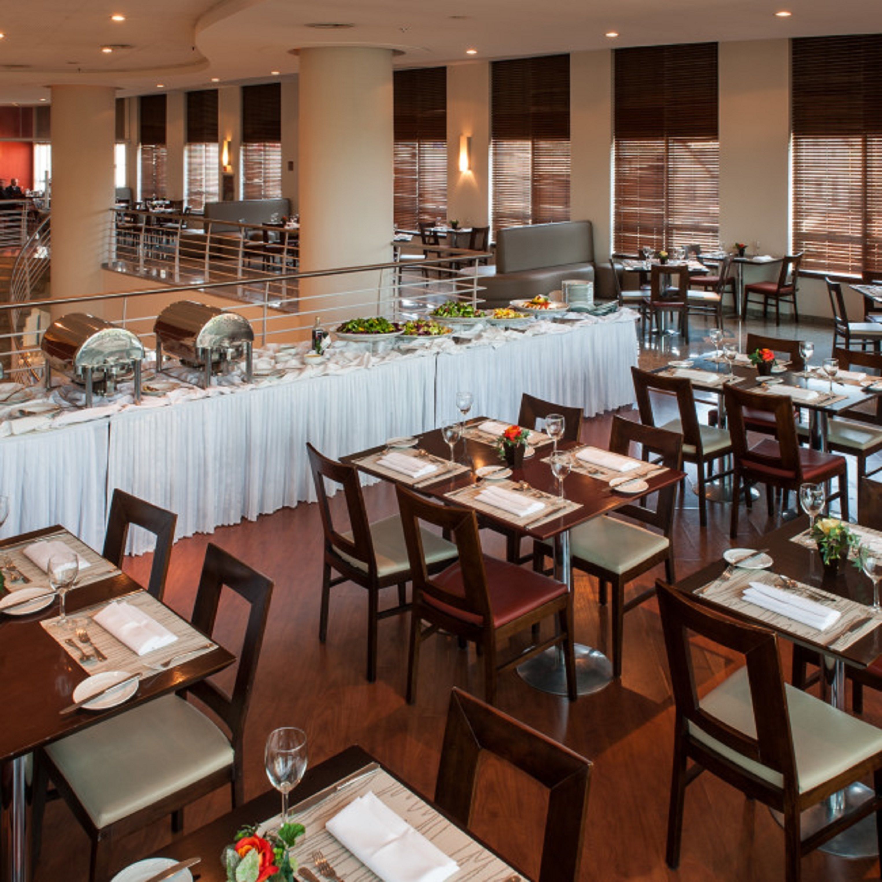 Un restaurante con varias mesas, sillas y una zona de bufé con distintos platos.