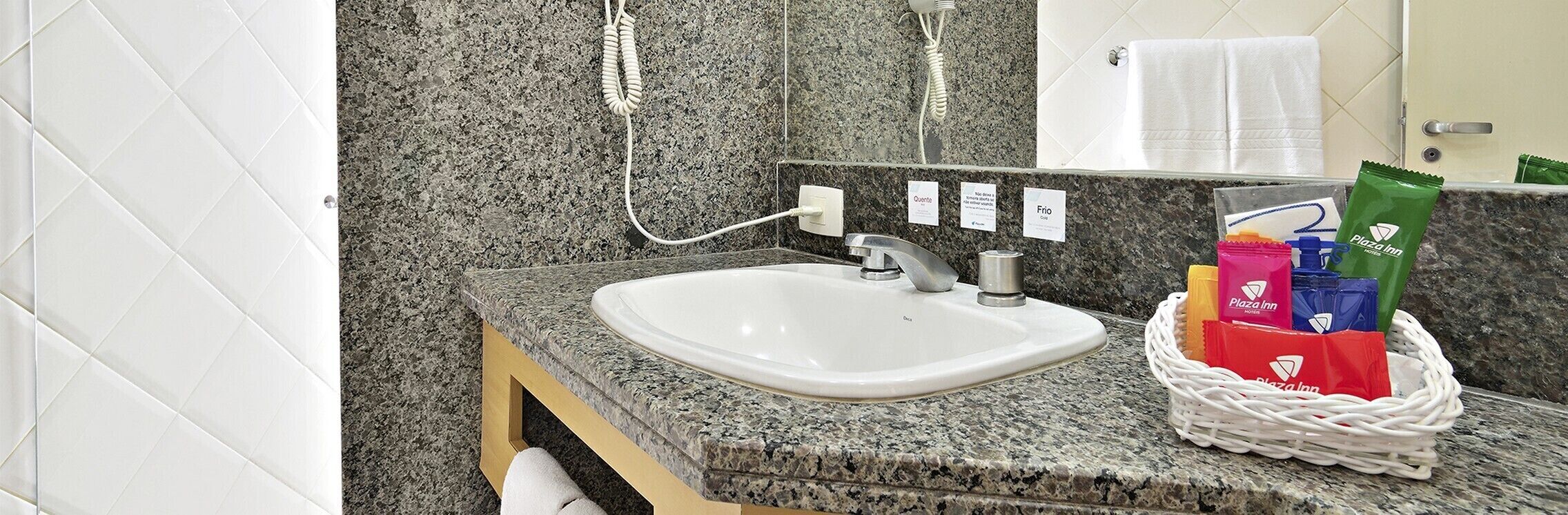 Un baño con encimera de granito, un lavamanos blanco, un perchero y una cesta de artículos de aseo.