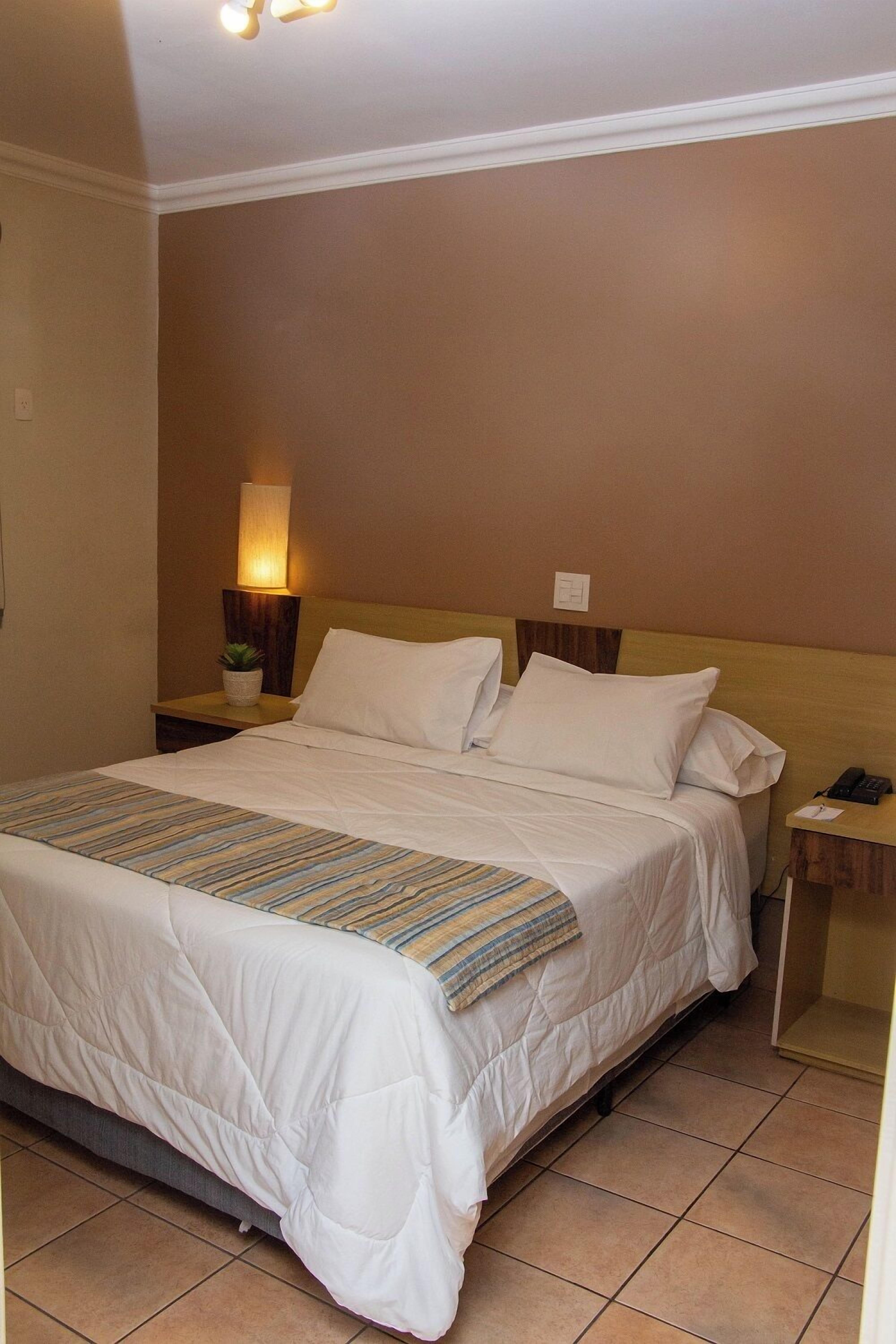 A hotel room with a bed, a bedside lamp, a nightstand, and a wall-mounted light fixture.
