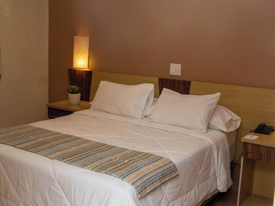 Una habitación de hotel con cama, lámpara de noche, mesita de noche e iluminación en la pared.