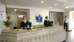 Una recepción con dos empleados, una planta y un cartel.