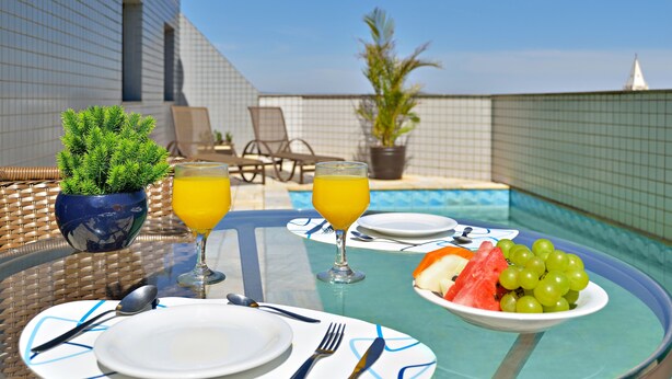 Una mesa de comedor con platos, cubiertos y un cuenco de fruta junto a una piscina.