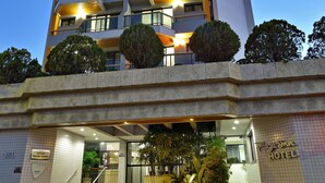 Un hotel de varios pisos con un diseño moderno, que cuenta con balcones en cada planta, una entrada visible con escaleras y un letrero que indica el nombre del hotel.