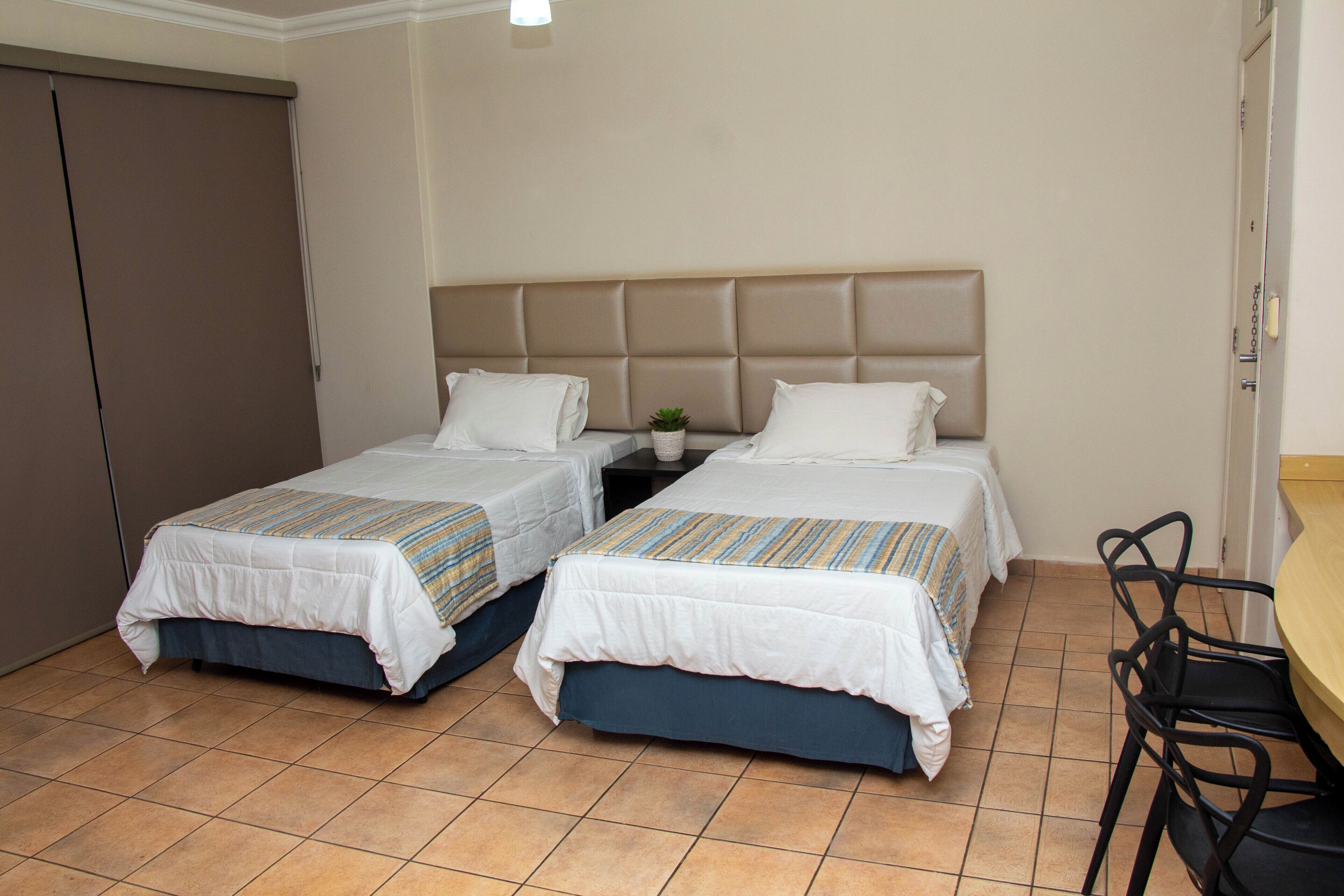 A hotel room with two single beds, a small table, a chair, and a door.