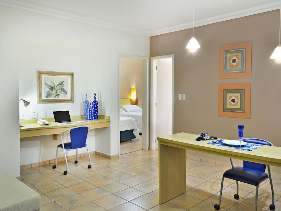 A hotel room with a desk, chair, bed, and a small table with a vase.