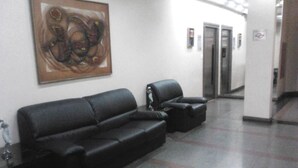 Un área de espera con un sofá de cuero negro, una mesita y un cuadro en la pared.