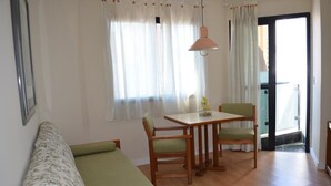 Una habitación con un sofá, una mesa de comedor con sillas, una lámpara colgante y un ventanal corredero que da a un balcón.